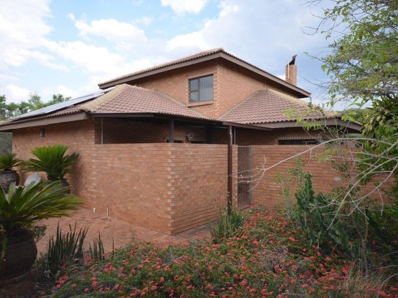 Rear view of a face brick house featuring a tiled roof, solar panels, and a private brick-paved patio area surrounded by established garden landscaping.