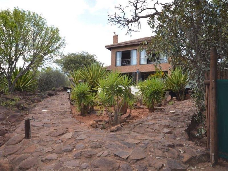 A view of the rear brick facade of the house, featuring a stone pathway leading through a landscaped garden area.