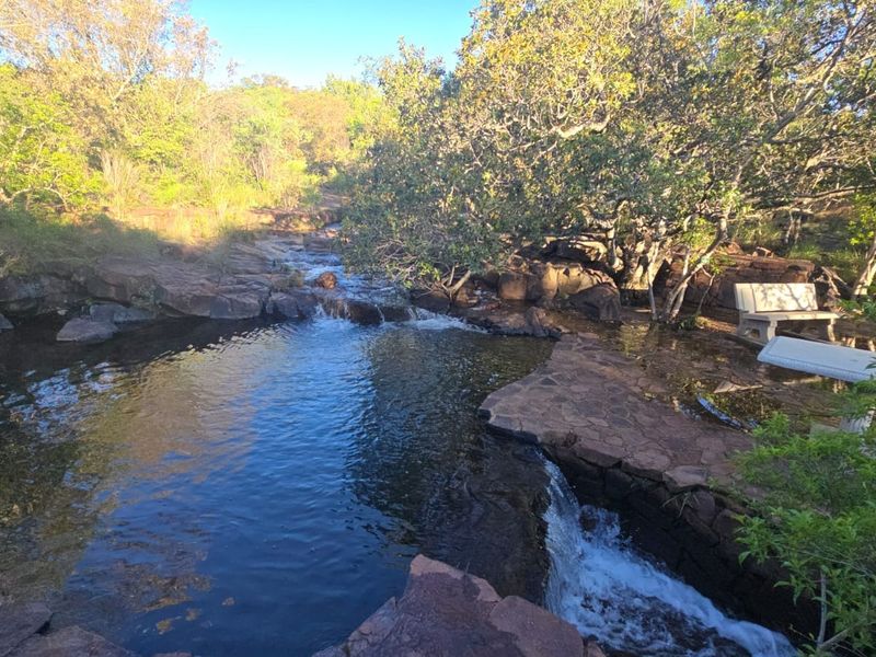 A scenic natural rock pool and waterfall feature set within a lush, landscaped garden environment.