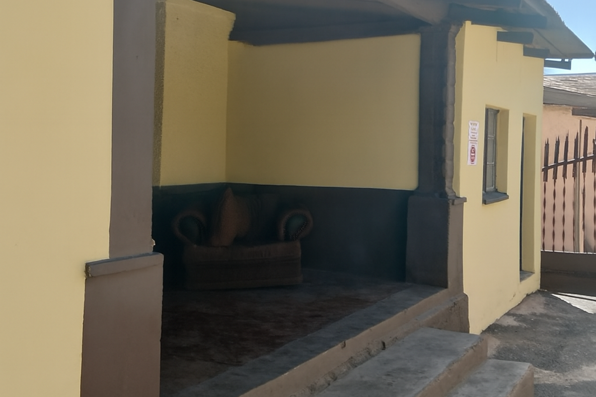 A covered outdoor porch area featuring concrete steps and exposed timber rafters, requiring minor maintenance to the exterior paint and masonry.