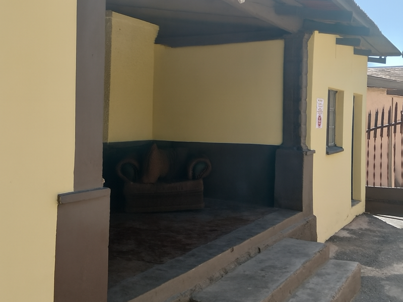 A covered outdoor porch area featuring concrete steps and exposed timber rafters, requiring minor maintenance to the exterior paint and masonry.