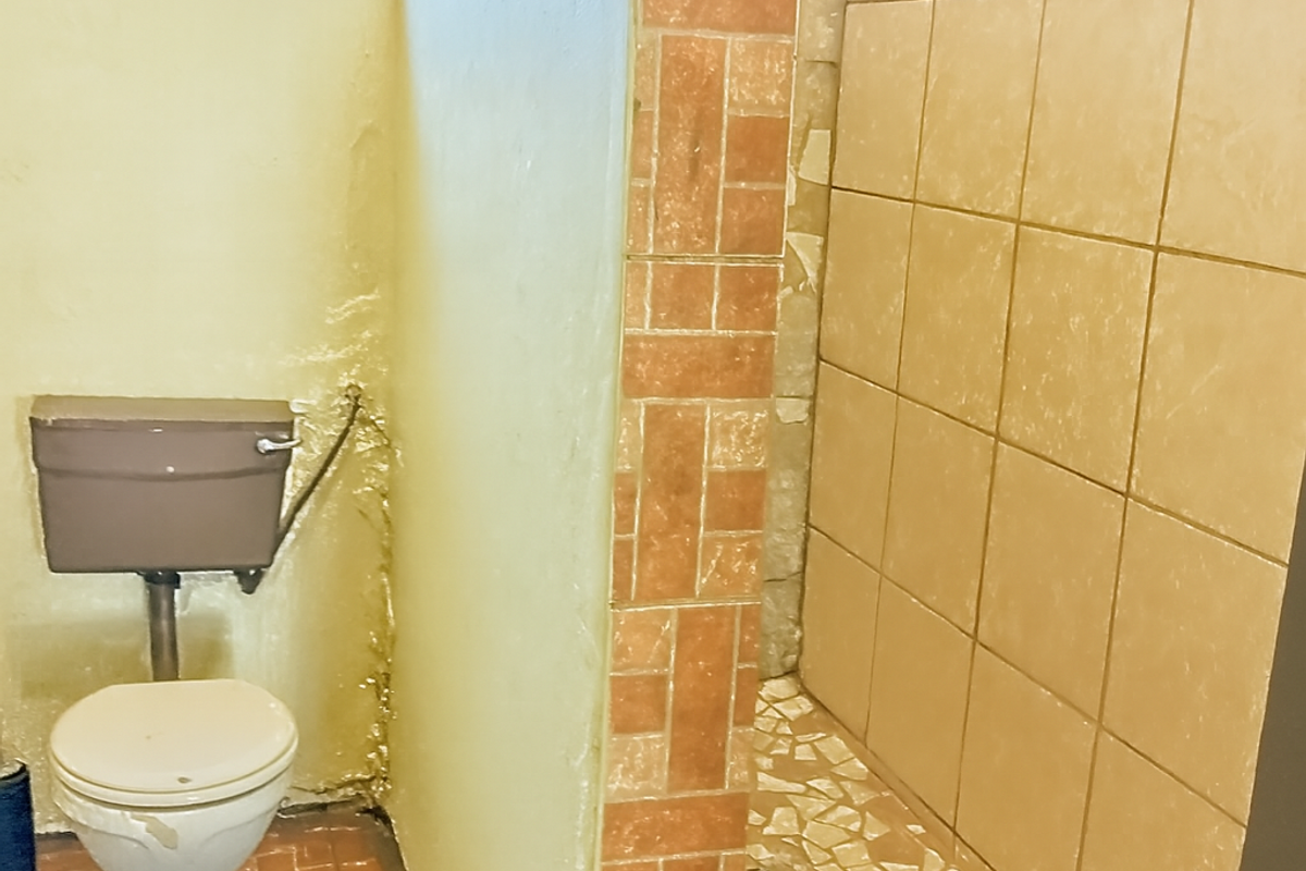 A dated bathroom featuring a separate shower enclosure with tiled finishes and a standard toilet, requiring cosmetic updates and modernization.