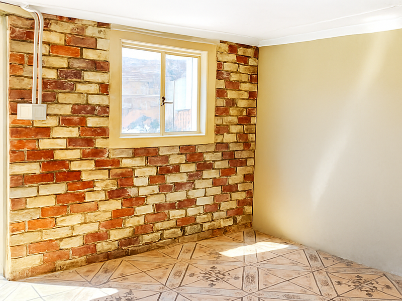 An empty room featuring an exposed brick accent wall, patterned ceramic floor tiles, and a sliding window with surface-mounted electrical wiring.