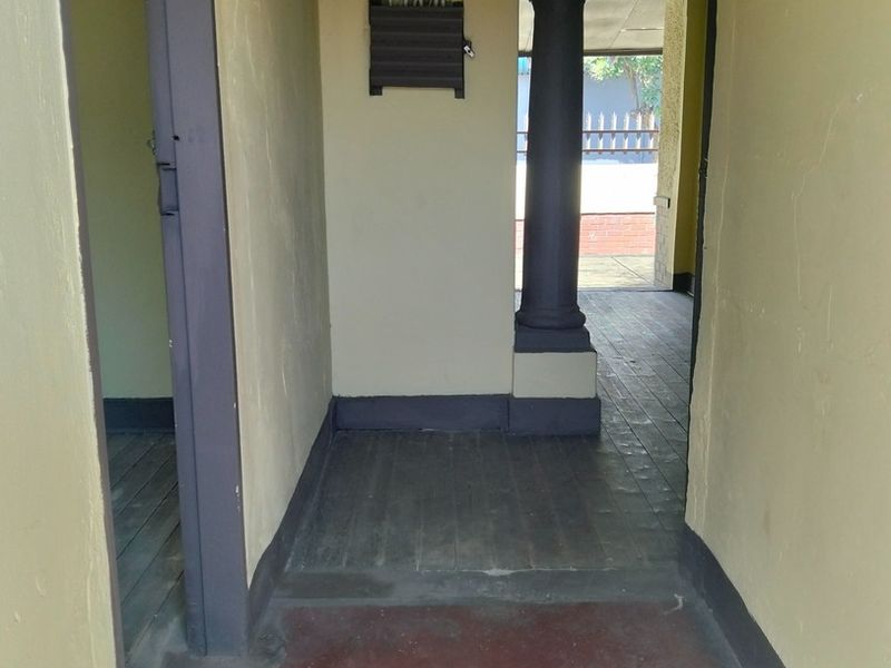 A functional hallway area featuring timber flooring, a structural column, and an exposed electrical distribution board, leading towards an outdoor patio space.