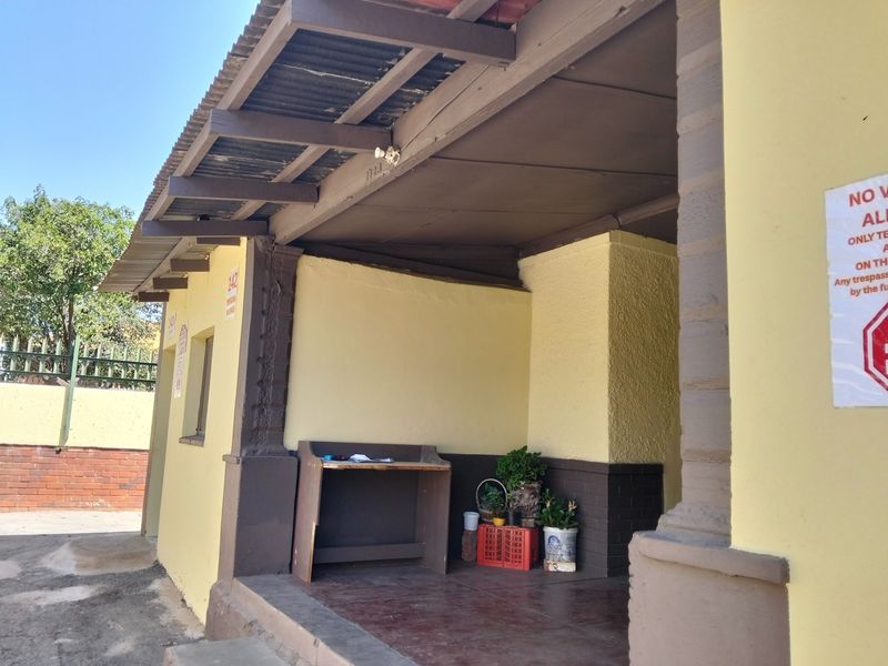 A covered outdoor patio area featuring exposed timber rafters, corrugated metal roofing, and brick support pillars, providing a functional sheltered entrance space.