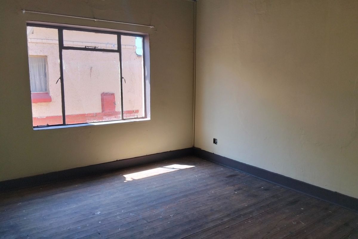 An empty bedroom featuring original timber flooring, steel-framed windows, and dark painted skirting boards, requiring cosmetic updates to restore its appeal.