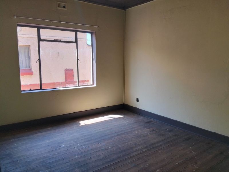 An empty bedroom featuring original timber flooring, steel-framed windows, and dark painted skirting boards, requiring cosmetic updates to restore its appeal.