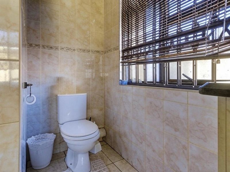 A functional bathroom featuring tiled walls and flooring, equipped with a standard toilet and a window fitted with security bars.