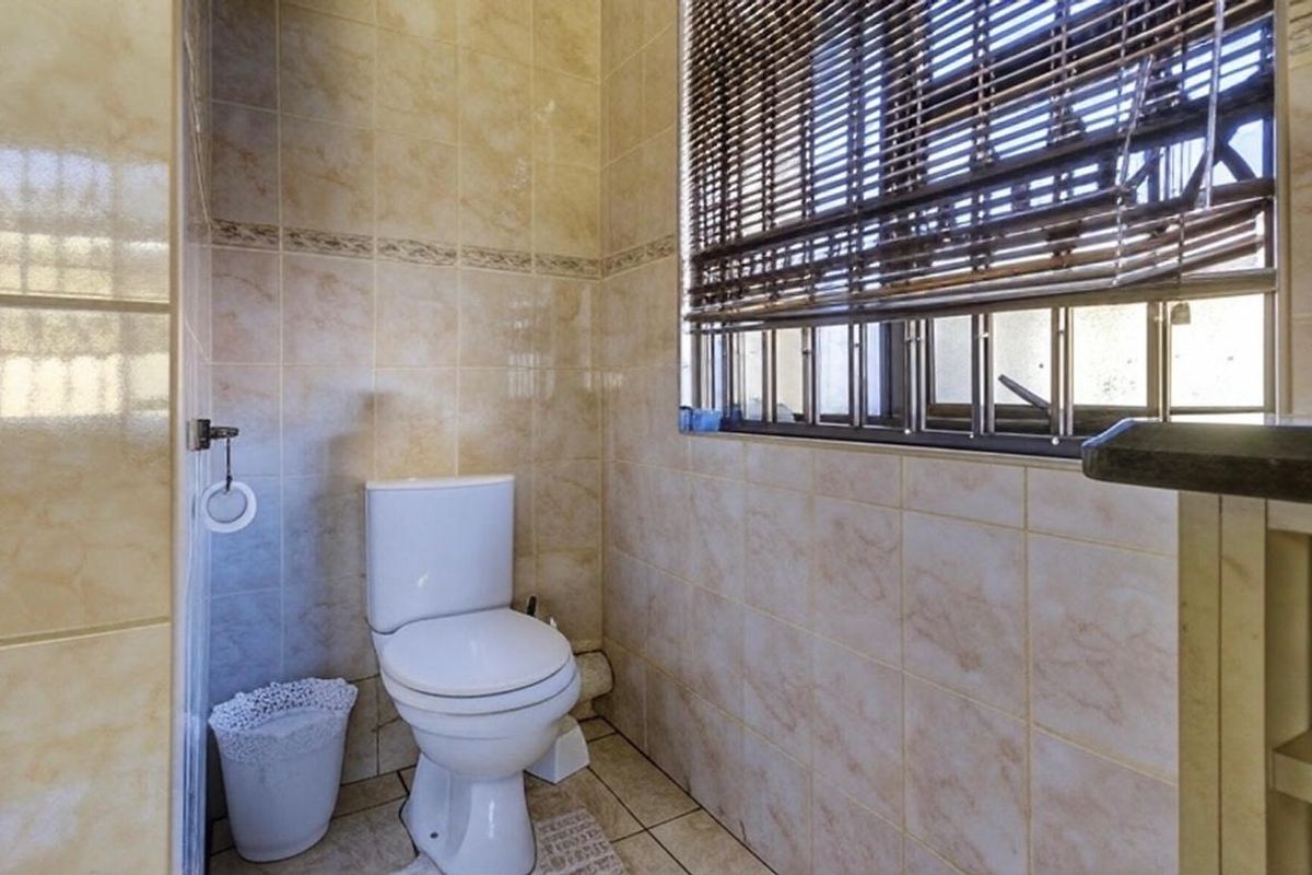A functional bathroom featuring tiled walls and flooring, equipped with a standard toilet and a window fitted with security bars.