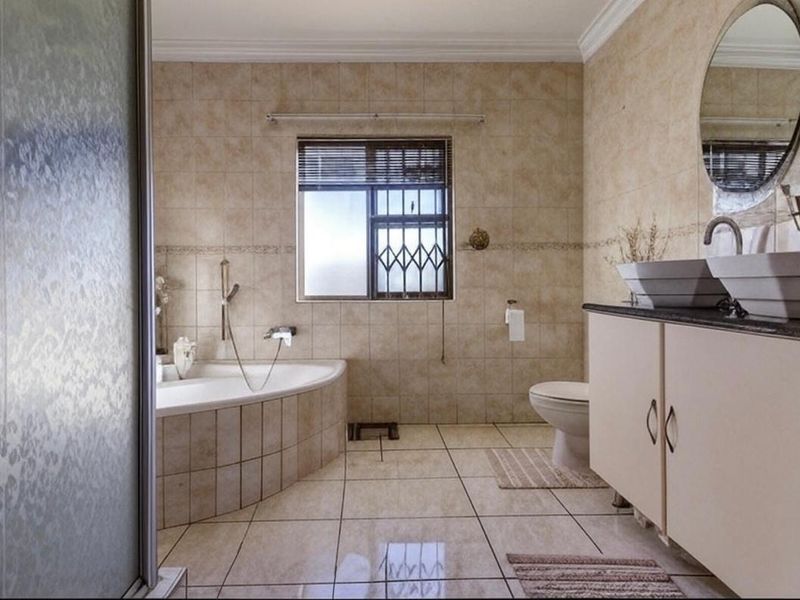A spacious bathroom featuring a corner bathtub, dual vessel sinks on a vanity cabinet, and neutral tiled finishes throughout.