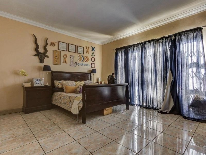 Spacious bedroom featuring tiled flooring, crown molding, and a sliding glass door with an integrated security gate providing access to the exterior.