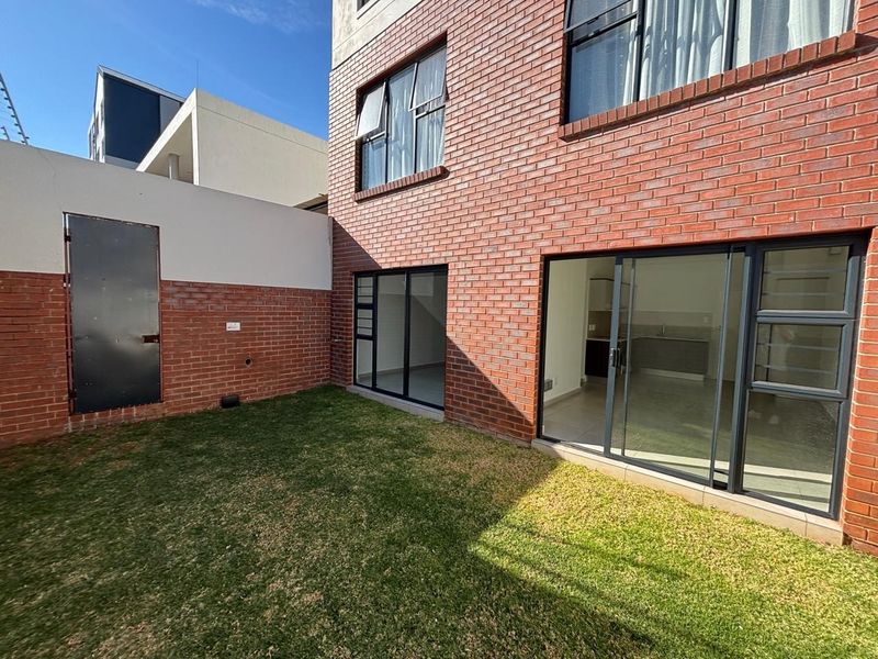 A private rear garden area featuring a well-maintained lawn, exposed brick exterior walls, and large sliding glass doors providing access to the interior.