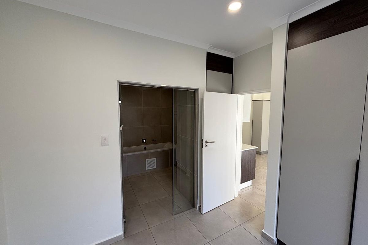 Spacious bedroom featuring neutral tiled flooring, built-in cupboards, and direct access to an en-suite bathroom with a glass door entry.