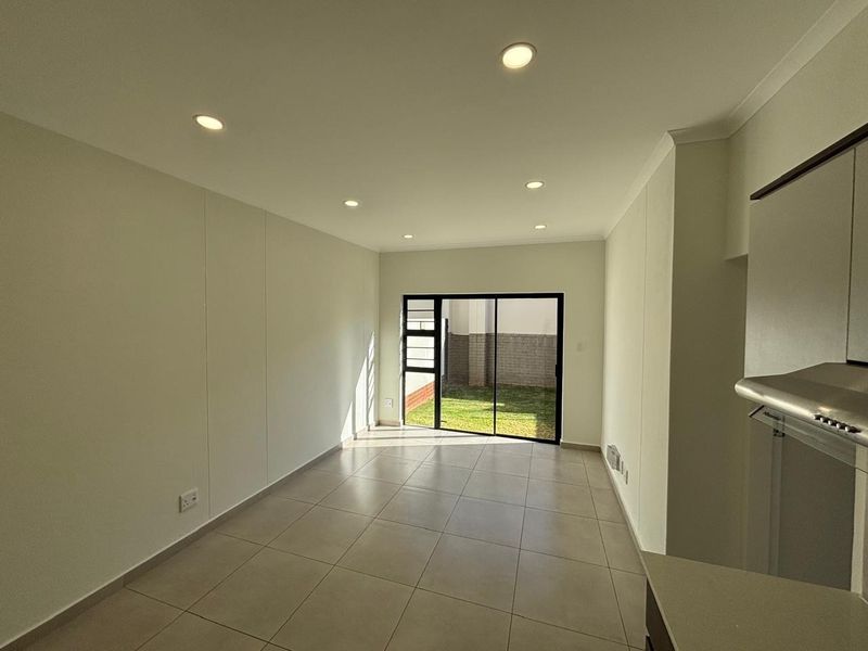 An open-plan living area featuring neutral tiled flooring, recessed downlights, and a sliding glass door providing direct access to the rear garden.