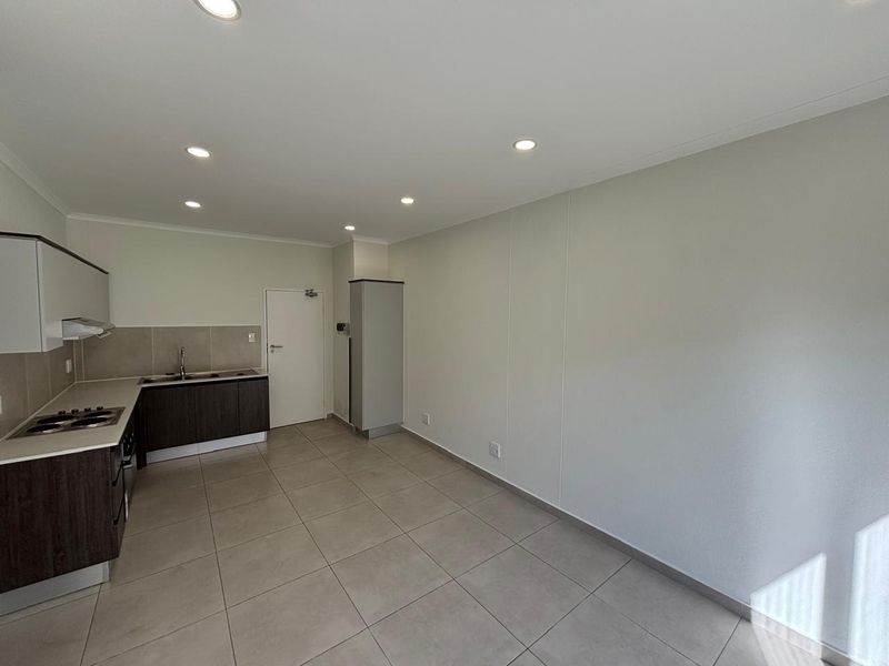 Modern open-plan kitchen and living area featuring neutral tiled flooring, contemporary cabinetry, integrated hob, and recessed downlighting in a clean, vacant space.