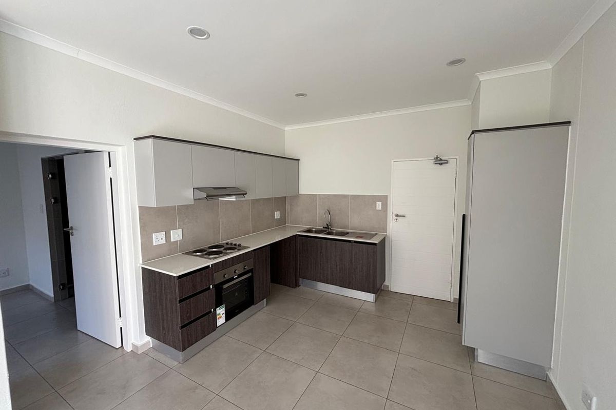 A clean, modern kitchen featuring two-tone cabinetry, built-in oven and hob, tiled splashbacks, and neutral floor tiles in an open-plan layout.
