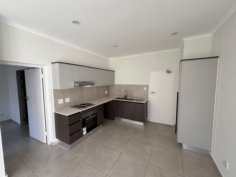 A clean, modern kitchen featuring two-tone cabinetry, built-in oven and hob, tiled splashbacks, and neutral floor tiles in an open-plan layout.