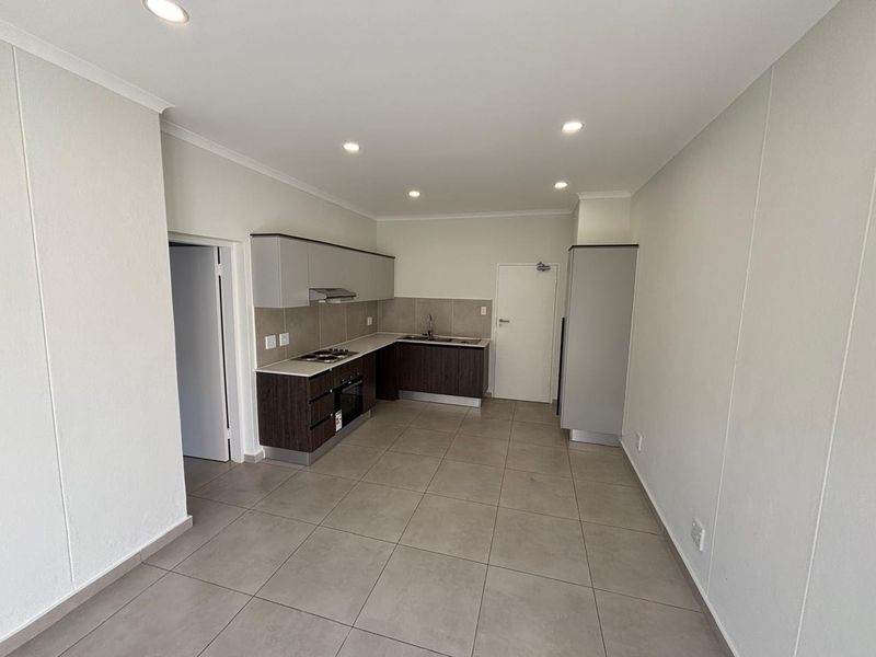 A modern, empty kitchen featuring dark and light cabinetry, built-in oven and hob, tiled flooring, and recessed lighting in a clean, neutral space.