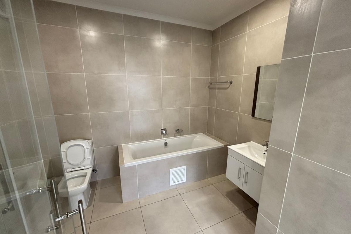 Modern bathroom featuring a built-in bathtub, wall-mounted vanity, toilet, and a glass-enclosed shower with neutral floor-to-ceiling tiling.