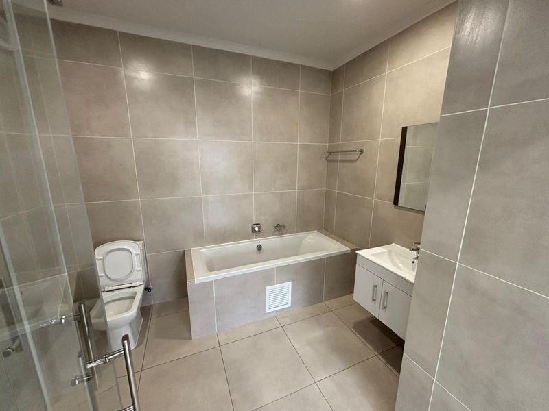 Modern bathroom featuring a built-in bathtub, wall-mounted vanity, toilet, and a glass-enclosed shower with neutral floor-to-ceiling tiling.