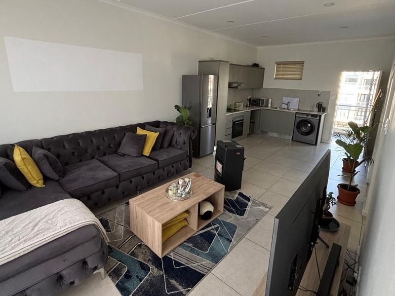Open-plan living area featuring a modern kitchen with built-in cabinetry, integrated appliances, and tiled flooring, seamlessly flowing into the lounge space.