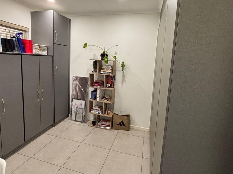 A functional utility space featuring extensive built-in grey cabinetry, neutral tiled flooring, and a window with venetian blinds.