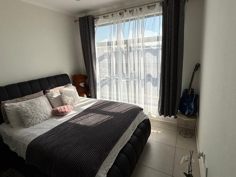 A well-lit bedroom featuring neutral tiled flooring and a large window with installed curtain tracks, providing ample natural light.