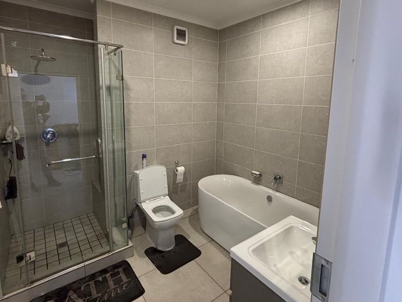 Modern bathroom featuring a glass-enclosed shower, a sleek freestanding bathtub, a wall-mounted toilet, and a vanity basin with neutral wall and floor tiling.