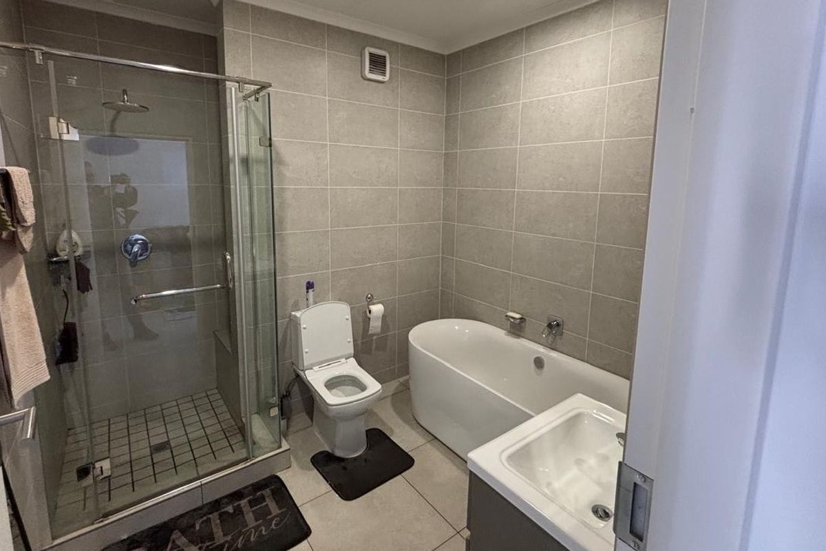 Modern bathroom featuring a glass-enclosed shower, a sleek freestanding bathtub, a wall-mounted toilet, and a vanity basin with neutral wall and floor tiling.
