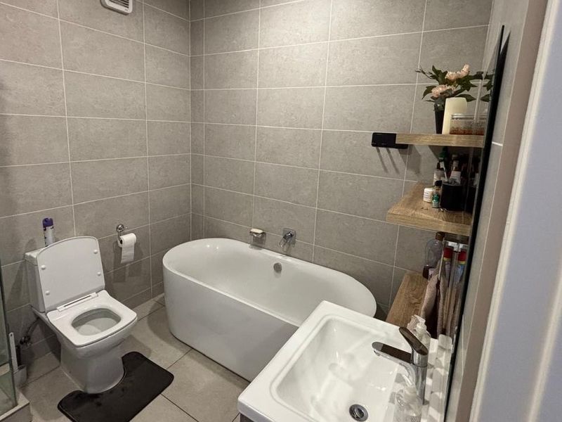Modern bathroom featuring a freestanding bathtub, glass shower enclosure, wall-mounted toilet, and vanity basin with neutral grey wall tiling.