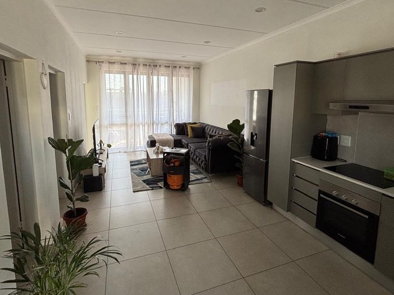 Modern open-plan living area featuring a sleek kitchen with built-in appliances, tiled flooring, and direct access to a balcony through sliding glass doors.