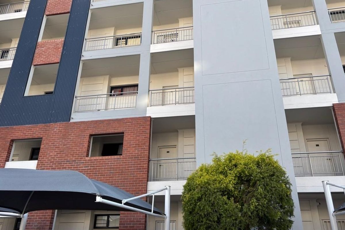Exterior view of a modern apartment building featuring multi-level balconies with metal railings, brick accents, and contemporary cladding.