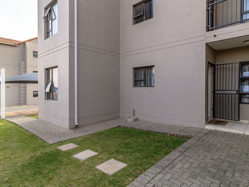 Exterior view of an apartment building featuring a paved walkway, small lawn area, and secure entrance with a metal security gate.