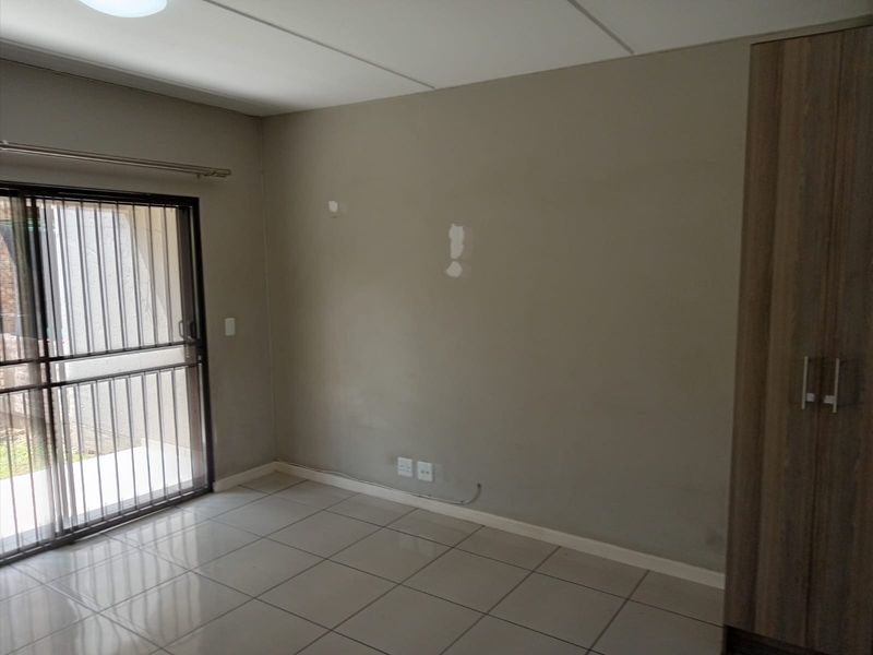 An empty bedroom featuring tiled flooring, a built-in wardrobe, and a sliding glass door with a security gate leading to the exterior.