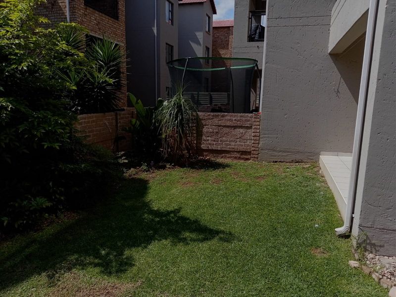 A private rear garden area featuring a small lawn, brick boundary wall, and a tiled patio section adjacent to the apartment building.