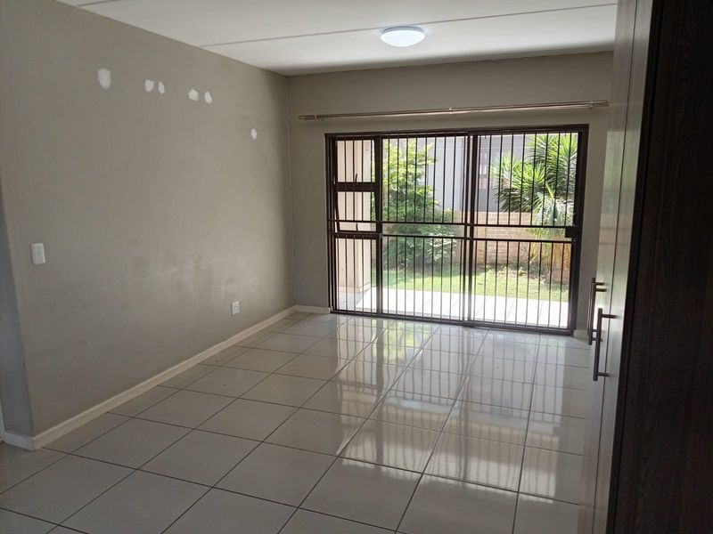 An empty living room featuring tiled flooring, a sliding glass door with security gate, and access to an outdoor area.
