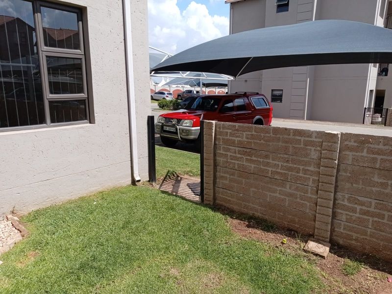 A view of the rear exterior area featuring a brick boundary wall, a metal gate, and a shade sail structure.