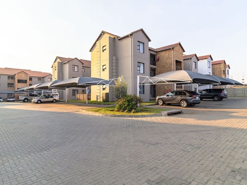 Exterior view of a modern apartment complex featuring paved parking areas with shade cloth carports and well-maintained building facades.