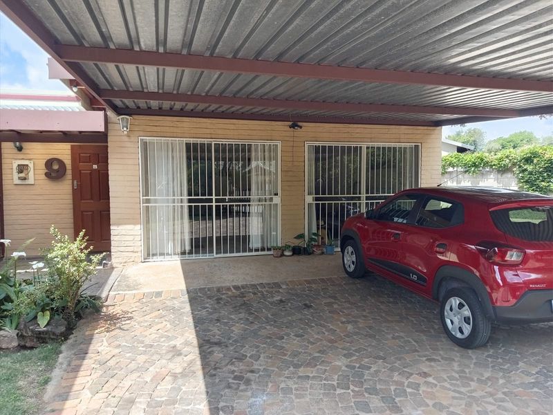 Front exterior view of the cottage featuring a covered carport, paved driveway, and secure sliding door access to the main living area.