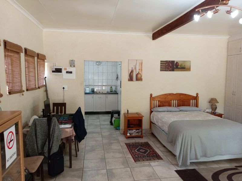 Open-plan studio cottage featuring tiled flooring, exposed timber ceiling beam, built-in bedroom cupboards, and a compact kitchenette area.
