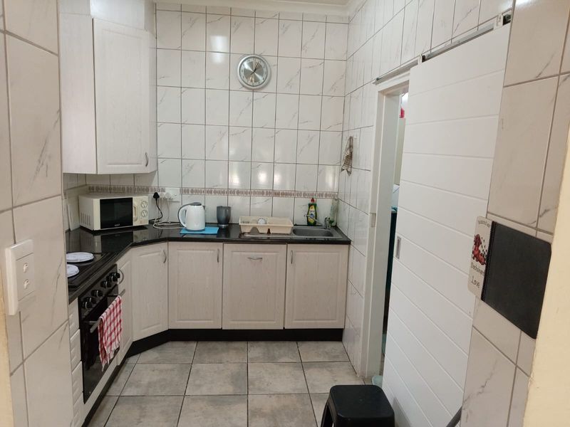 A functional kitchen featuring light-toned cabinetry, dark granite countertops, tiled walls and flooring, and a convenient sliding door entry.