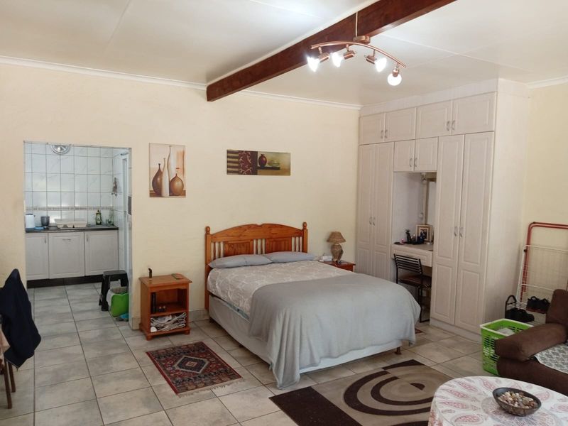 Spacious bedroom featuring built-in cupboards, a vanity area, and an exposed timber ceiling beam, with direct access to an adjacent kitchen area.
