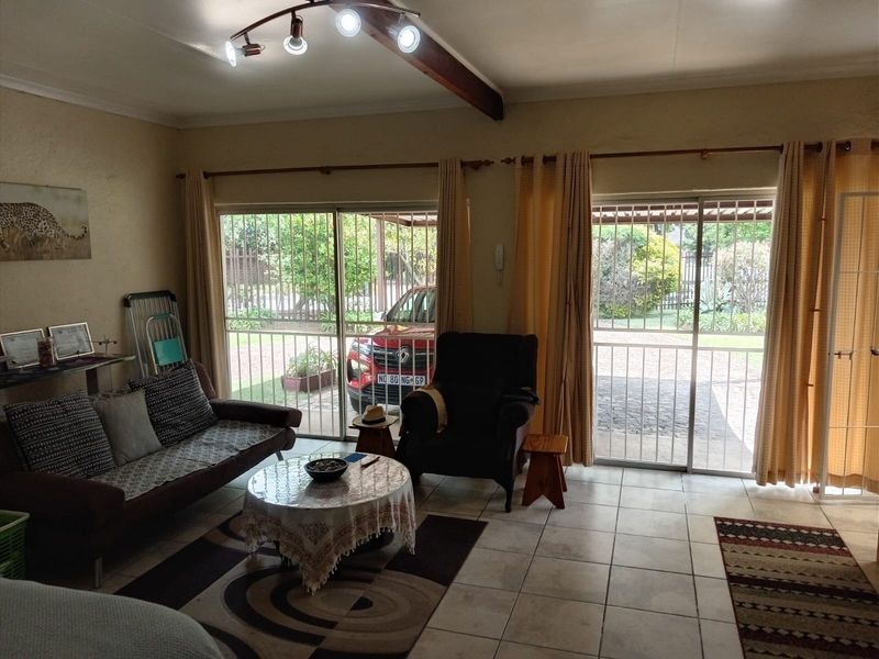 A living room featuring tiled flooring, an exposed timber ceiling beam, and sliding glass doors with security gates providing access to the exterior.