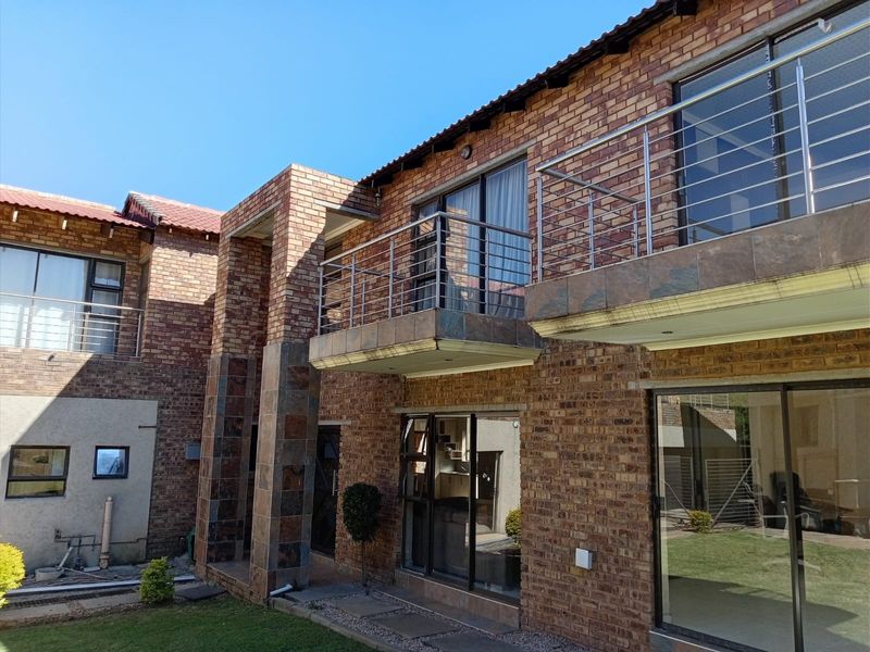 Rear elevation of a double-storey face brick house featuring a balcony with stainless steel railings and large sliding glass doors.