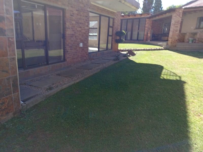 A view of the rear exterior featuring a face brick facade, large sliding glass doors, and a well-maintained lawn with a paved walkway.