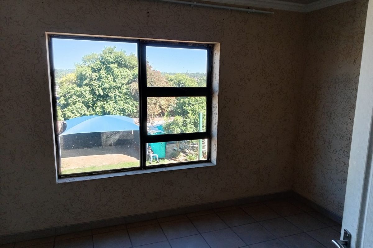 An empty bedroom featuring tiled flooring, textured walls, and an aluminium window frame overlooking the rear garden area.