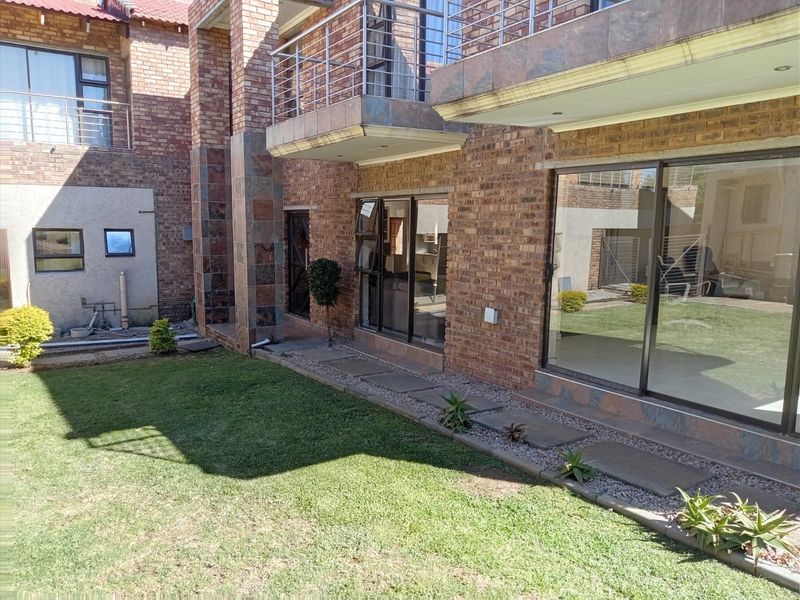 Rear view of a double-story face brick house featuring a landscaped garden, paved walkway, and an upper-level balcony with a stainless steel balustrade.