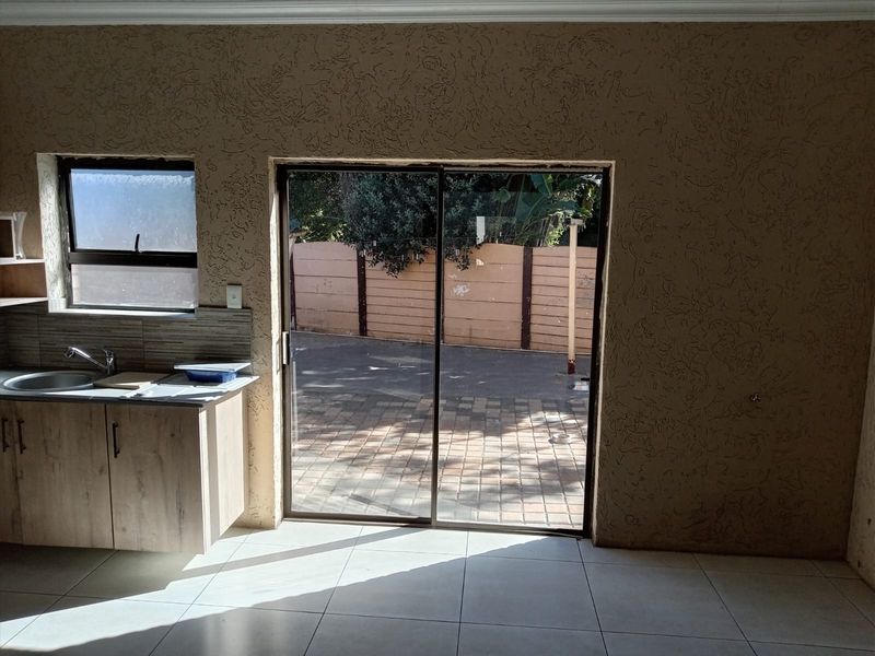 A compact kitchen area featuring built-in cabinetry, a stainless steel sink, and direct access to the outdoor patio through a sliding glass door.
