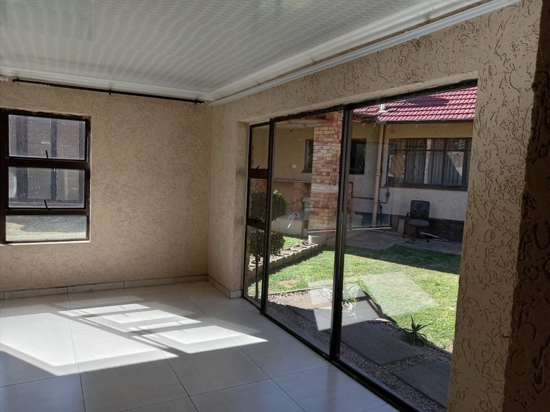 An empty, sunlit living area featuring tiled flooring, textured walls, and large sliding glass doors providing direct access to the rear garden.