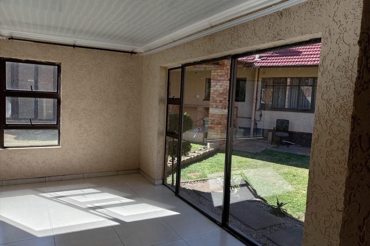 An empty, sunlit living area featuring tiled flooring, textured walls, and large sliding glass doors providing direct access to the rear garden.